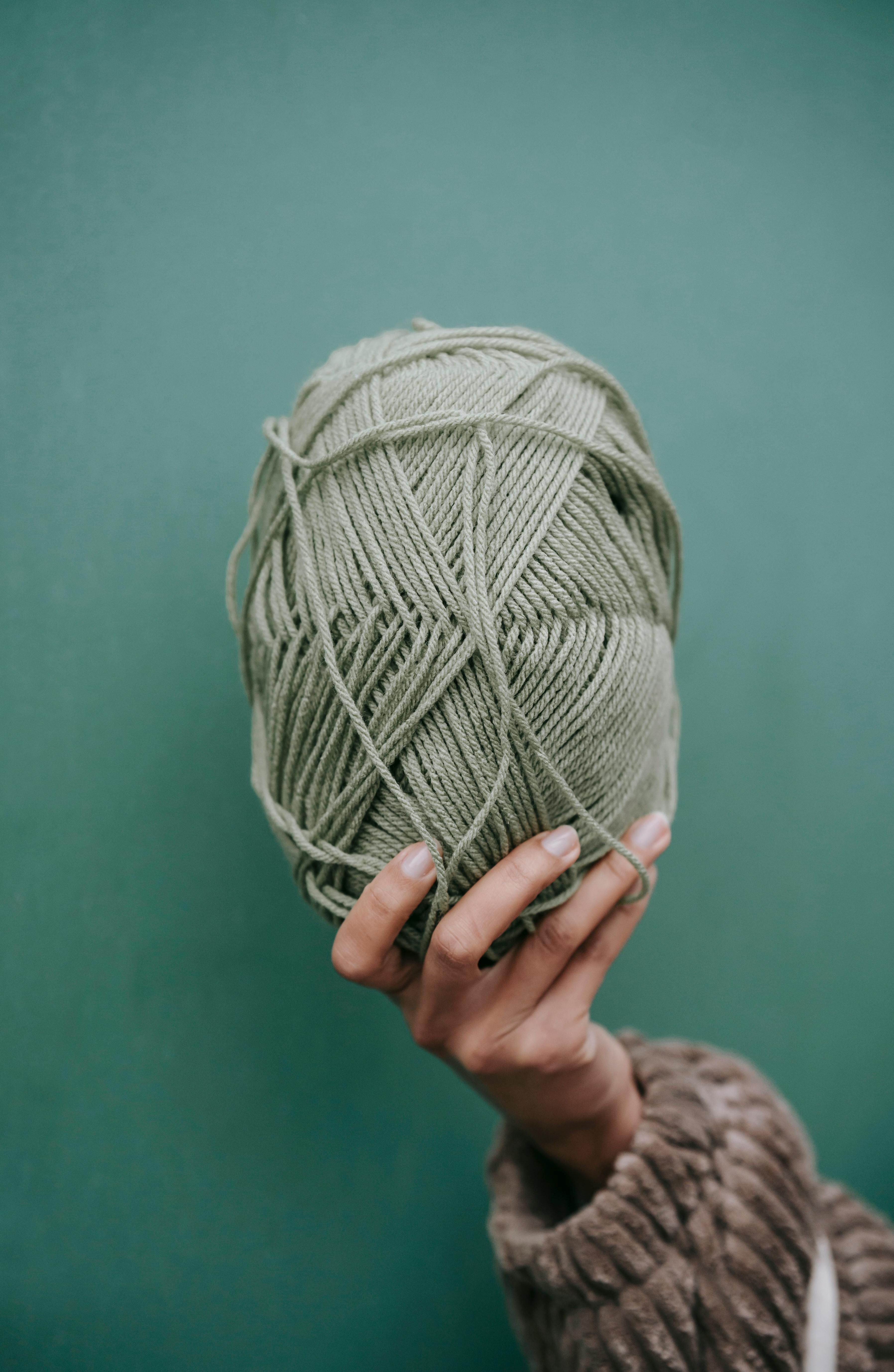 woman in sweater showing ball of yarn against green wall