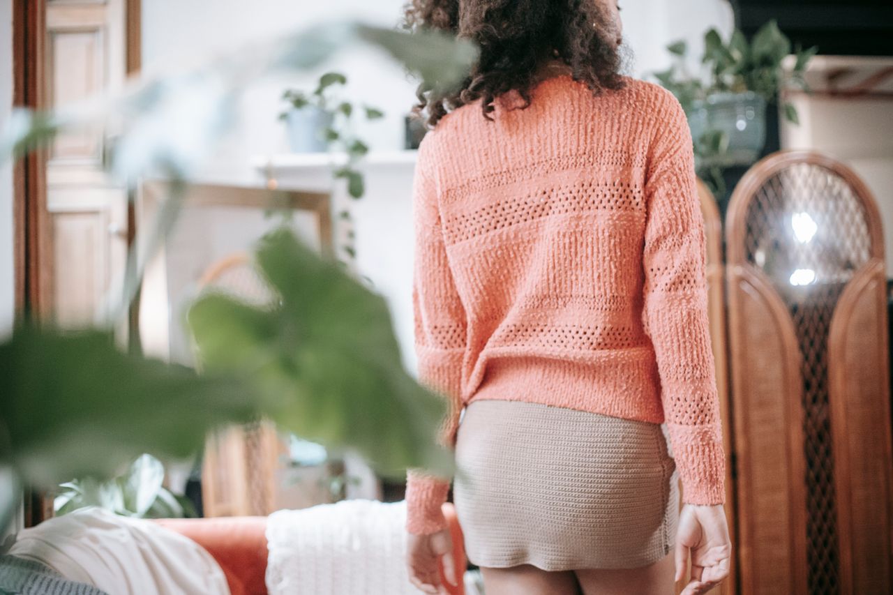 Back view of a woman wearing a coral knit sweater with a beige knit mini skirt