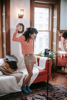 A young woman joyously dances in a cozy apartment while filming herself for social media content.
