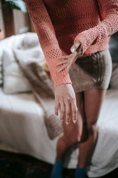 Crop unrecognizable ethnic female showing knitted outfit while standing by sofa at home