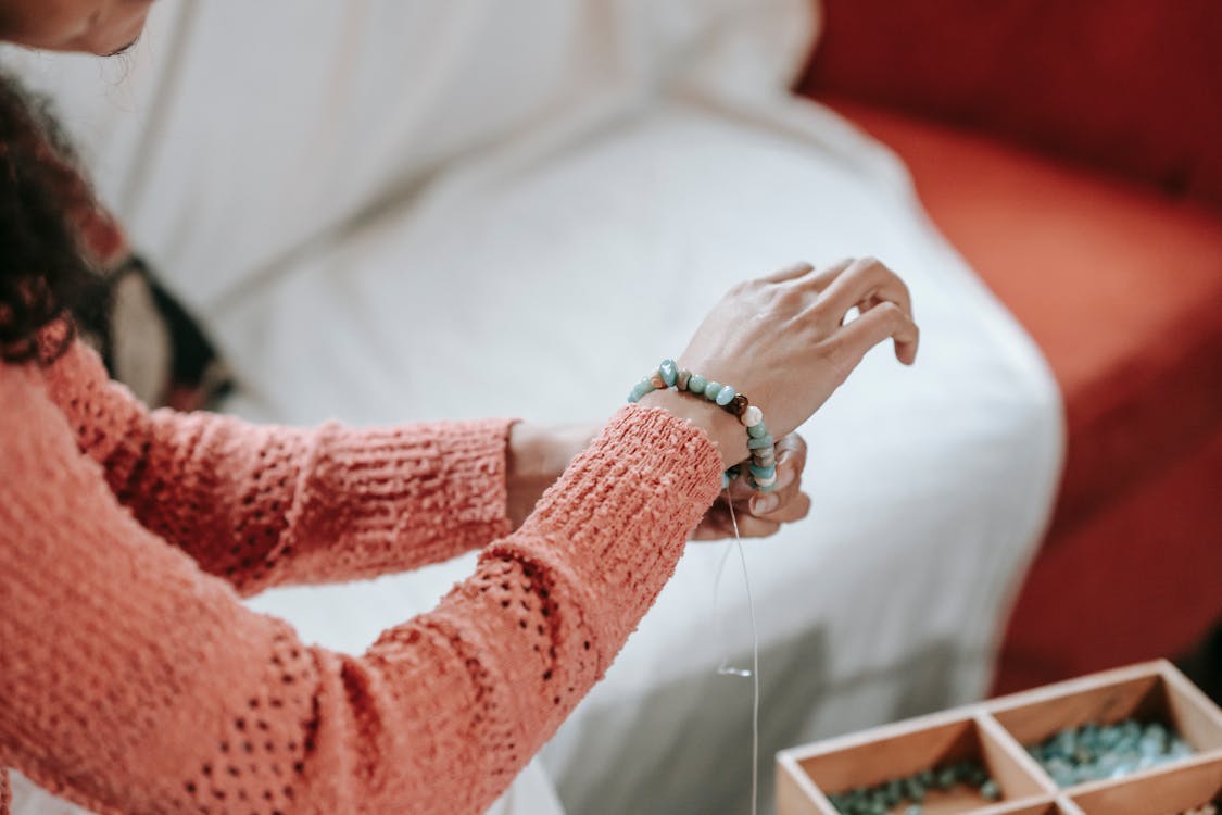 High angle of crop anonymous female designer tying decorative bracelet on wrist made of stones