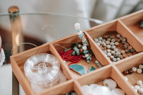 Wooden container with abundance of colorful beads and elastic cord for making bracelet placed on glass table in light room