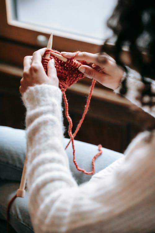 Side view of crop anonymous female artisan with yarn and needles knitting while having free time in house