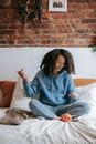 Smiling black artisan with yarn skein on bed at home