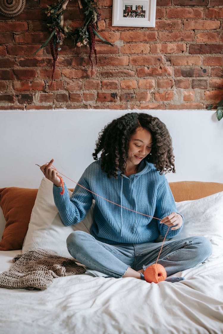 Smiling Black Artisan With Yarn Skein On Bed At Home