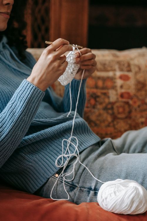 Free Side view of crop anonymous ethnic craftswoman with yarn ball and hook crocheting on couch in room Stock Photo