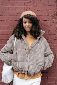 Young ethnic female with curly hair and hands in pockets looking at camera on street
