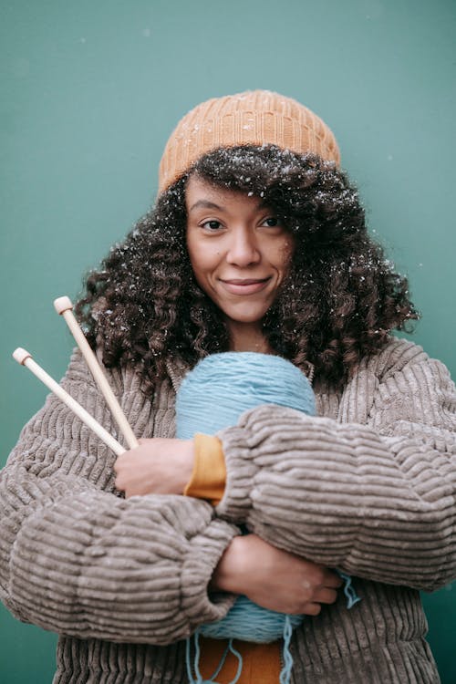 Smiling black artisan with yarn and knitting needles in winter