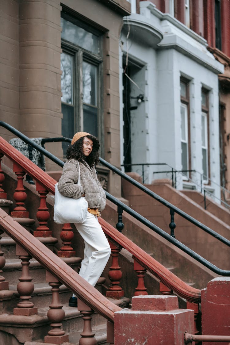 Black Woman In Outerwear With Cloth Bag On Urban Stairs