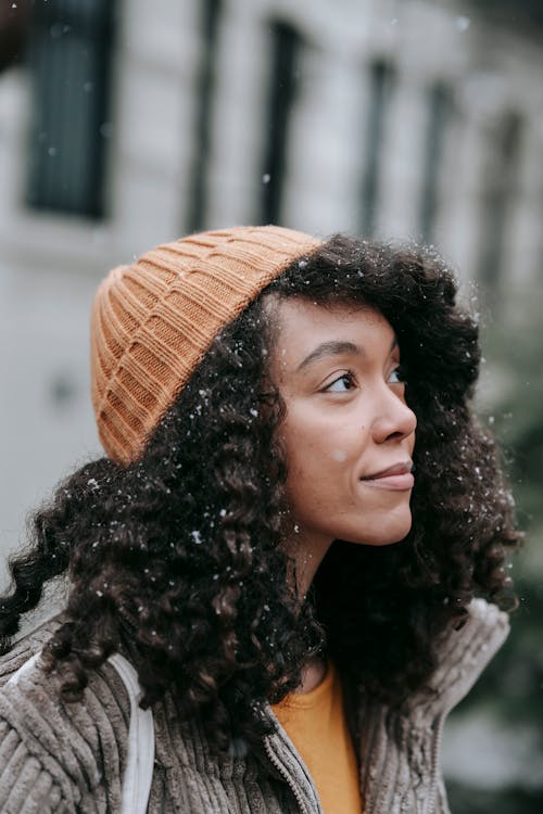 Free Contemplative young African American female in warm clothes with curly hair looking up on street in snowy weather Stock Photo