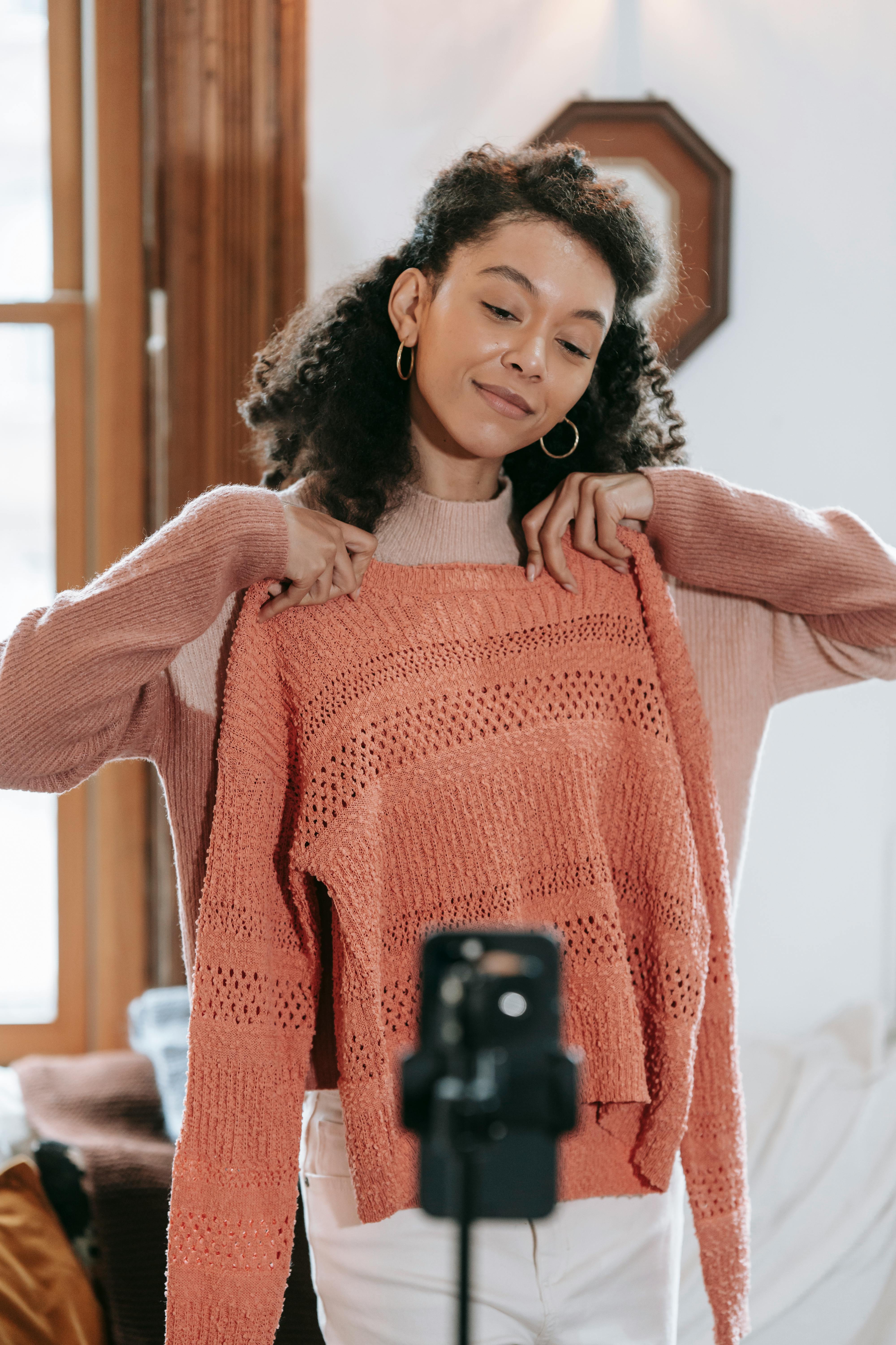 positive young woman trying on orange sweater and taking photo