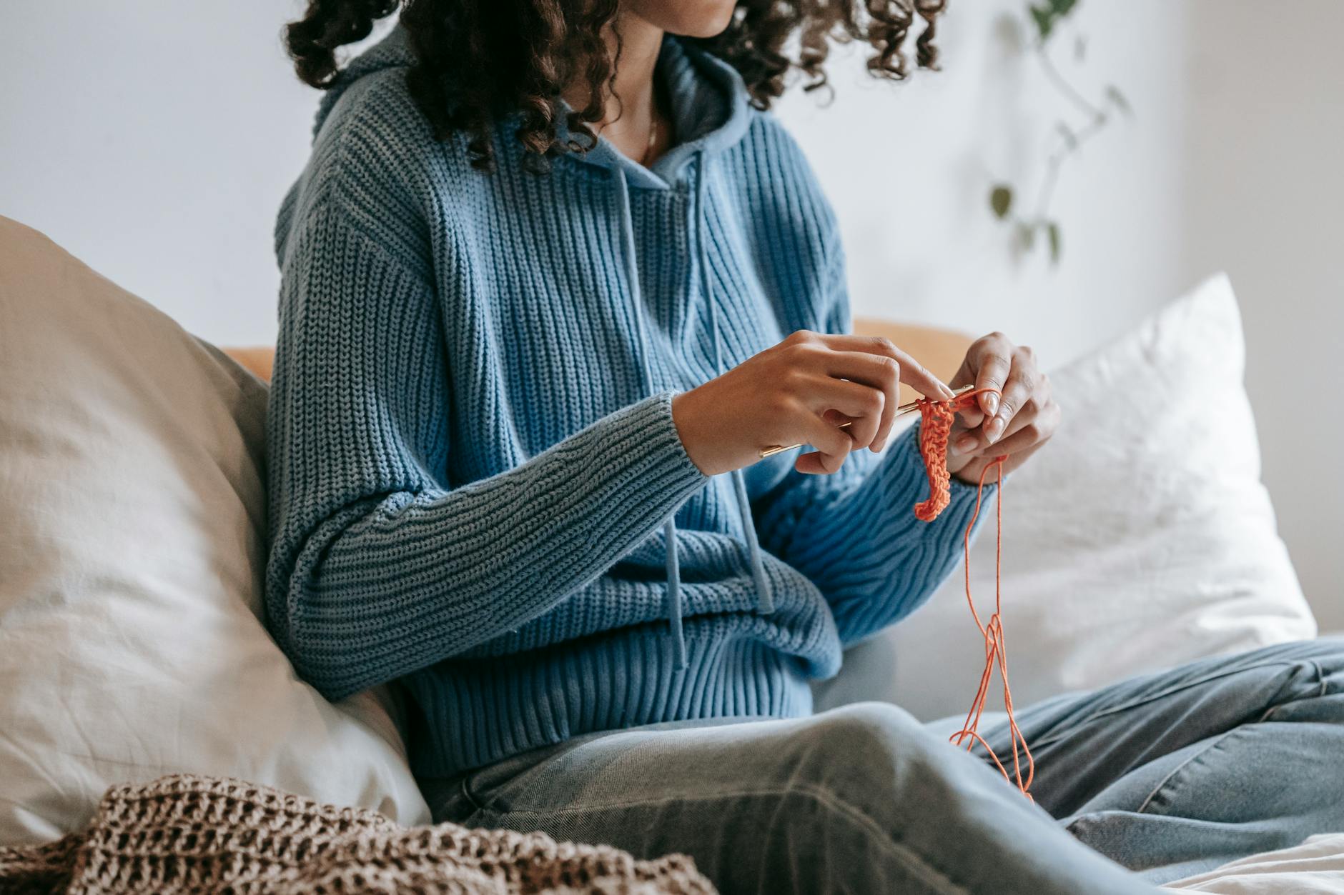 A woman relaxes at home crocheting, enjoying her leisure time in a cozy indoor setting.