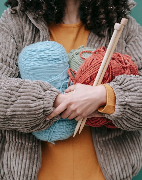 Crop anonymous female in warm sweater with knitting needles and skeins of multicolored yarns in hands