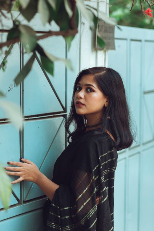Free Asian woman in black dress posing by a blue wall outdoors, looking over shoulder. Stock Photo