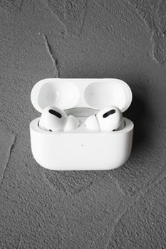 Close-up of white wireless earbuds in an open charging case on a textured surface.