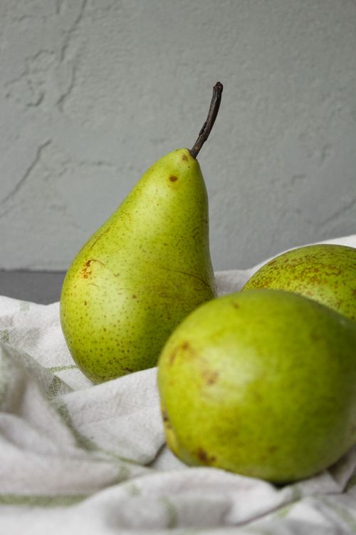Free Ripe green pears with brown spots placed on white textile on table near wall in bright place Stock Photo