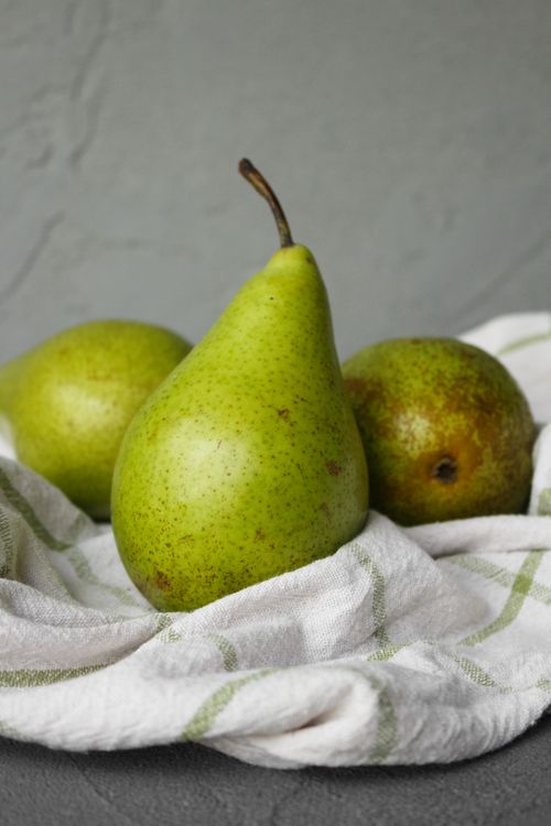 Free Fresh ripe green pears with brown spots placed on table on white fabric in light place near wall Stock Photo