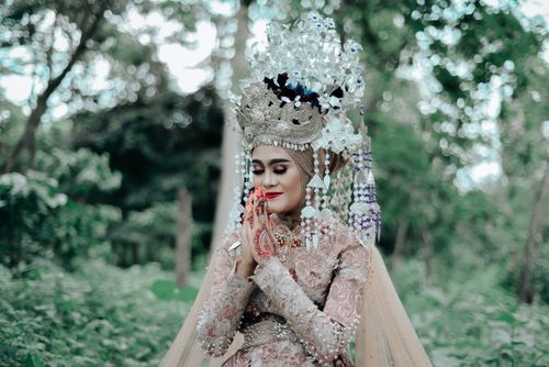 Free A woman in ornate traditional attire and headdress in a serene forest backdrop. Stock Photo