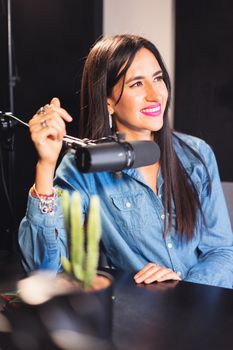 Cheerful woman podcast host in recording studio with microphone and denim shirt.