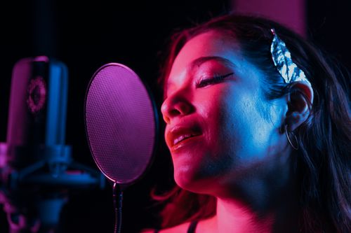 Free Close-up of a woman passionately singing into a studio microphone with vibrant lighting. Stock Photo