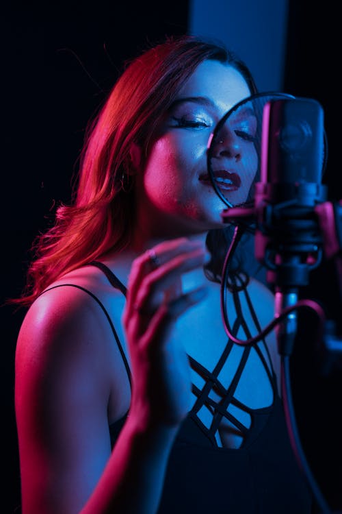 Free Pink Neon Light on Woman's Face while Singing on a Condenser Microphone Stock Photo