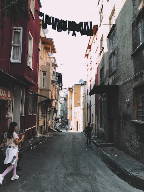 Free People strolling on narrow street with asphalt sidewalk and aged residential buildings with windows and canopies in poor district of town Stock Photo