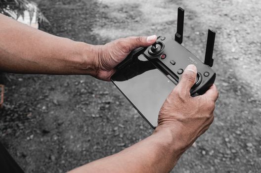 A person's hands holding a modern drone controller outdoors on a gravel surface day.