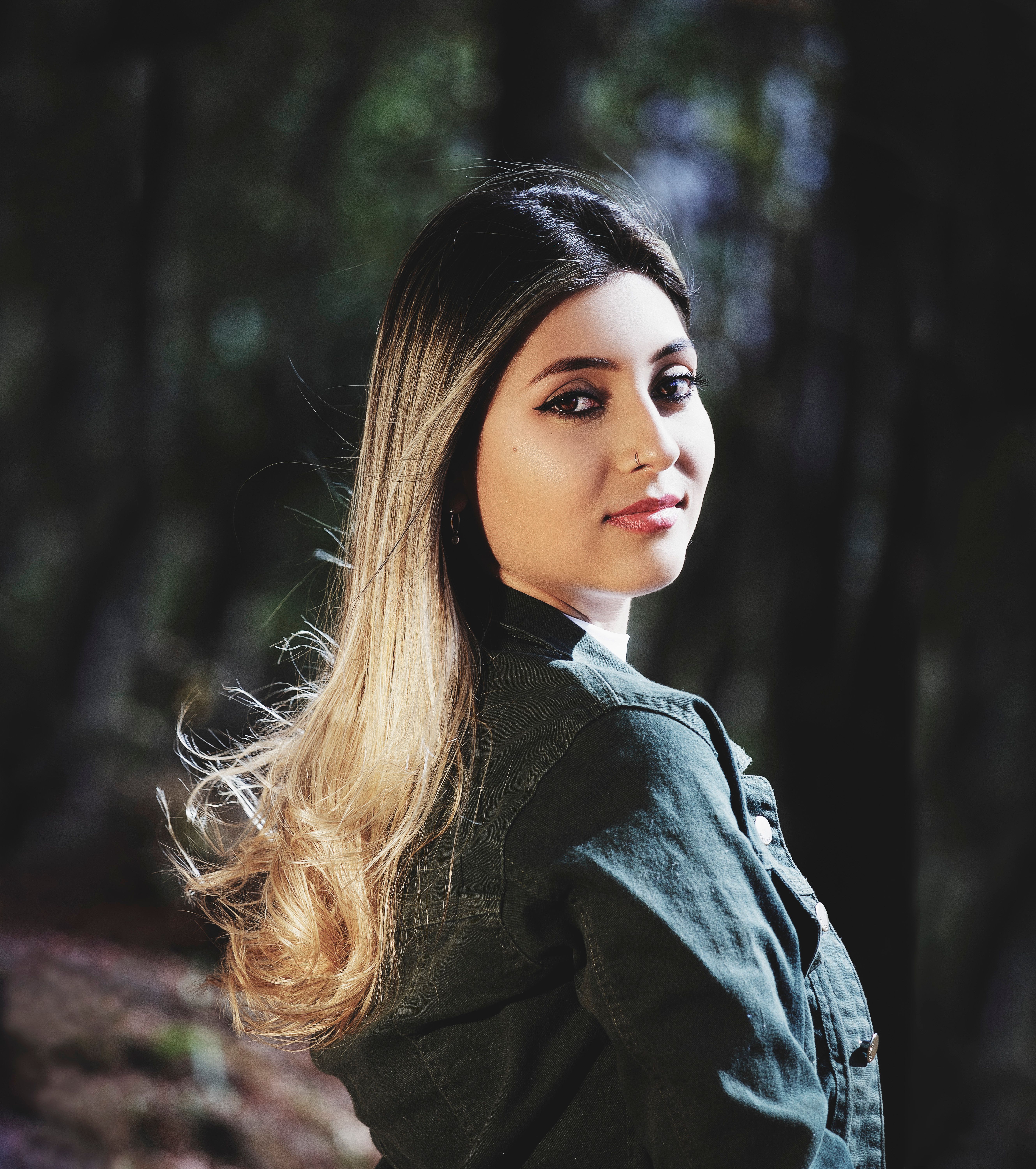 Elegant outdoor portrait of a woman with long blonde ombre hair, wearing a green jacket in natural light.