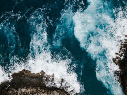 Free Dramatic aerial shot capturing the turquoise waves crashing against the rocky Maltese coastline. Stock Photo