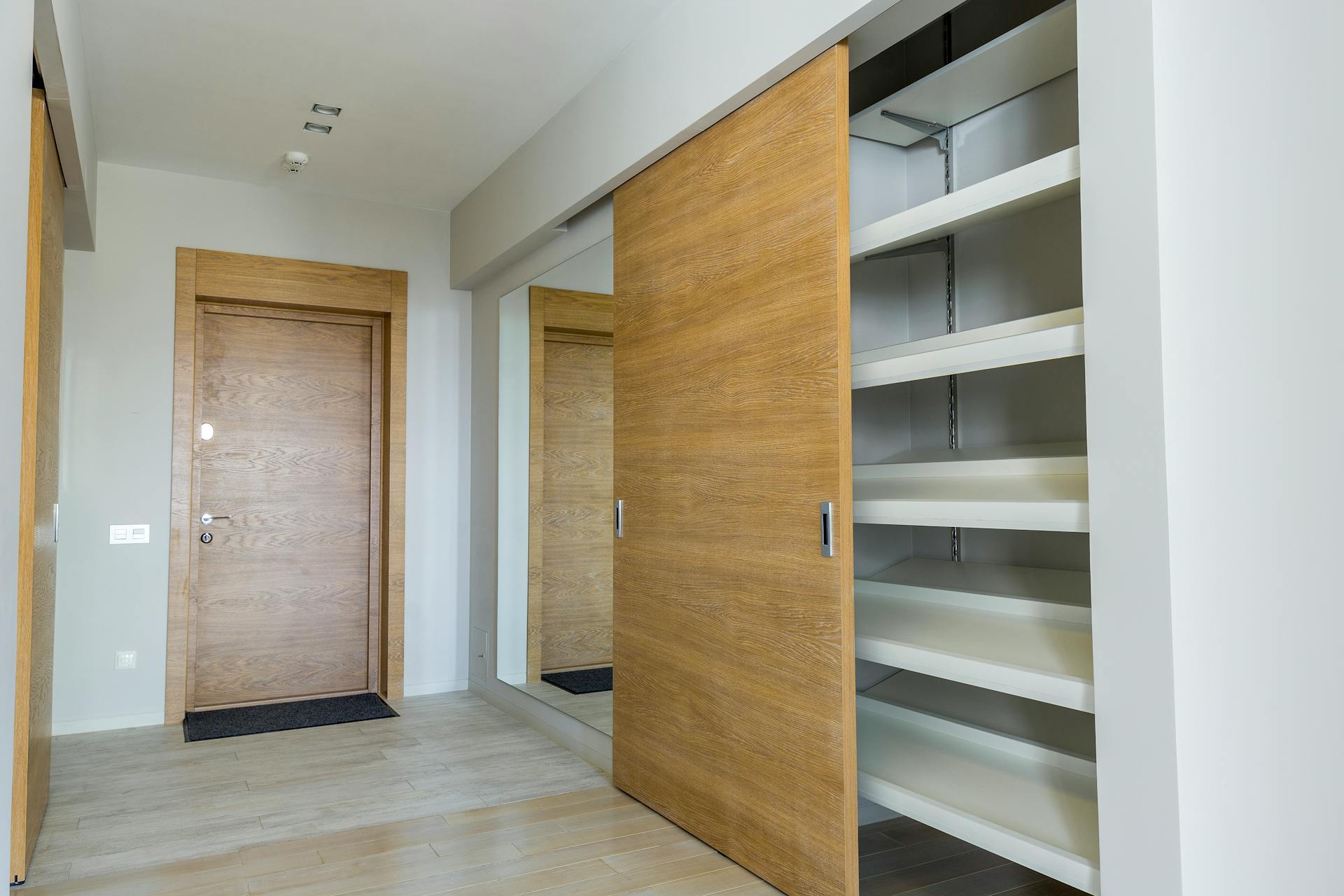 Elegant modern walk-in closet with wooden sliding door and empty shelves in a sleek minimalist style.