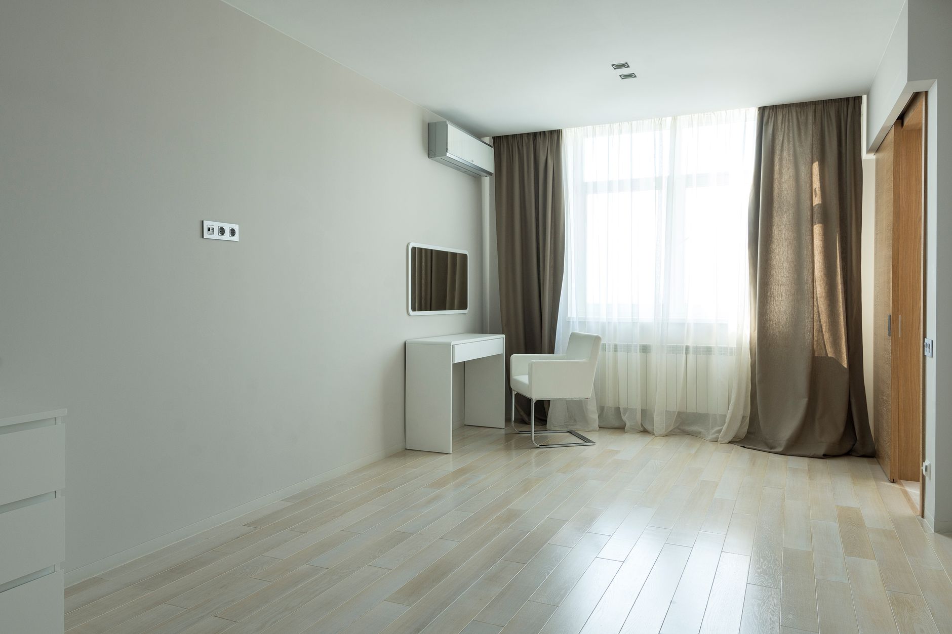 Spacious minimalist room with white furniture, curtains, and natural light.