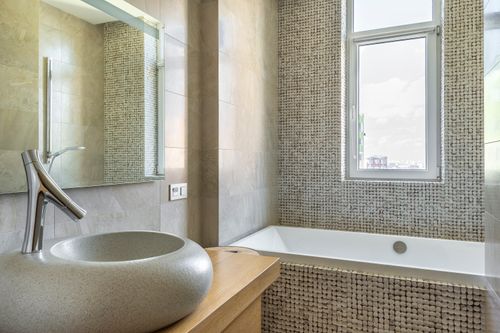 Free Elegant bathroom featuring a stone sink, modern faucet, and stylish bathtub with mosaic tiles. Stock Photo
