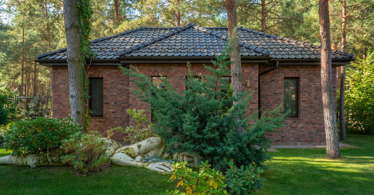A modern brick house surrounded by a lush forest and lawn, featuring serene outdoor landscaping.
