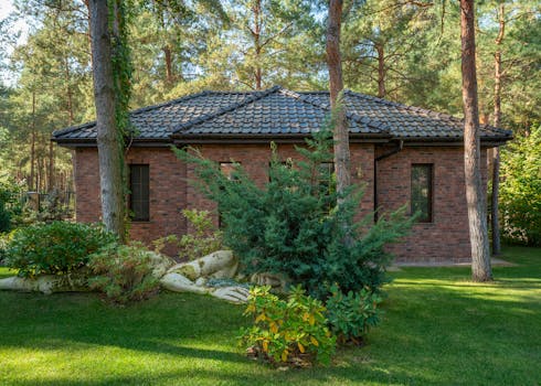 A modern brick house surrounded by a lush forest and lawn, featuring serene outdoor landscaping.