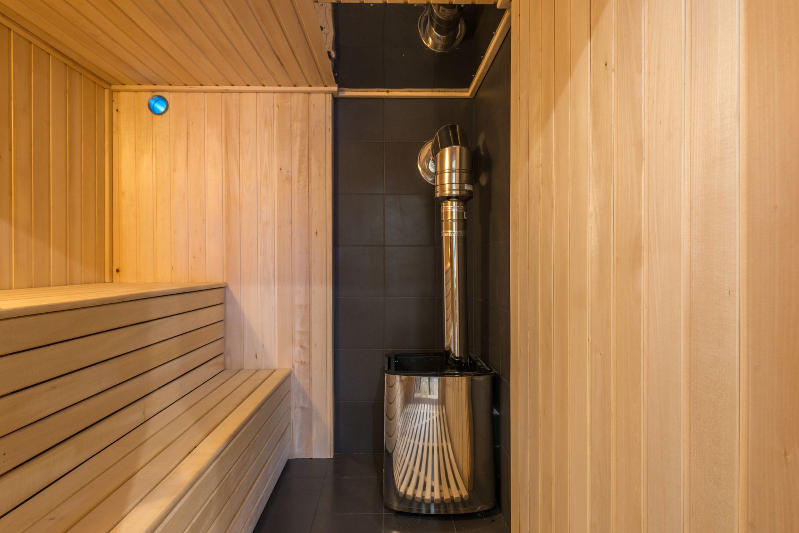 Modern home sauna interior with a sleek metal heater and clean timber walls.