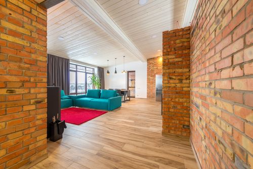 Free Spacious living room featuring brick walls, teal sofa, and large windows with natural light. Stock Photo