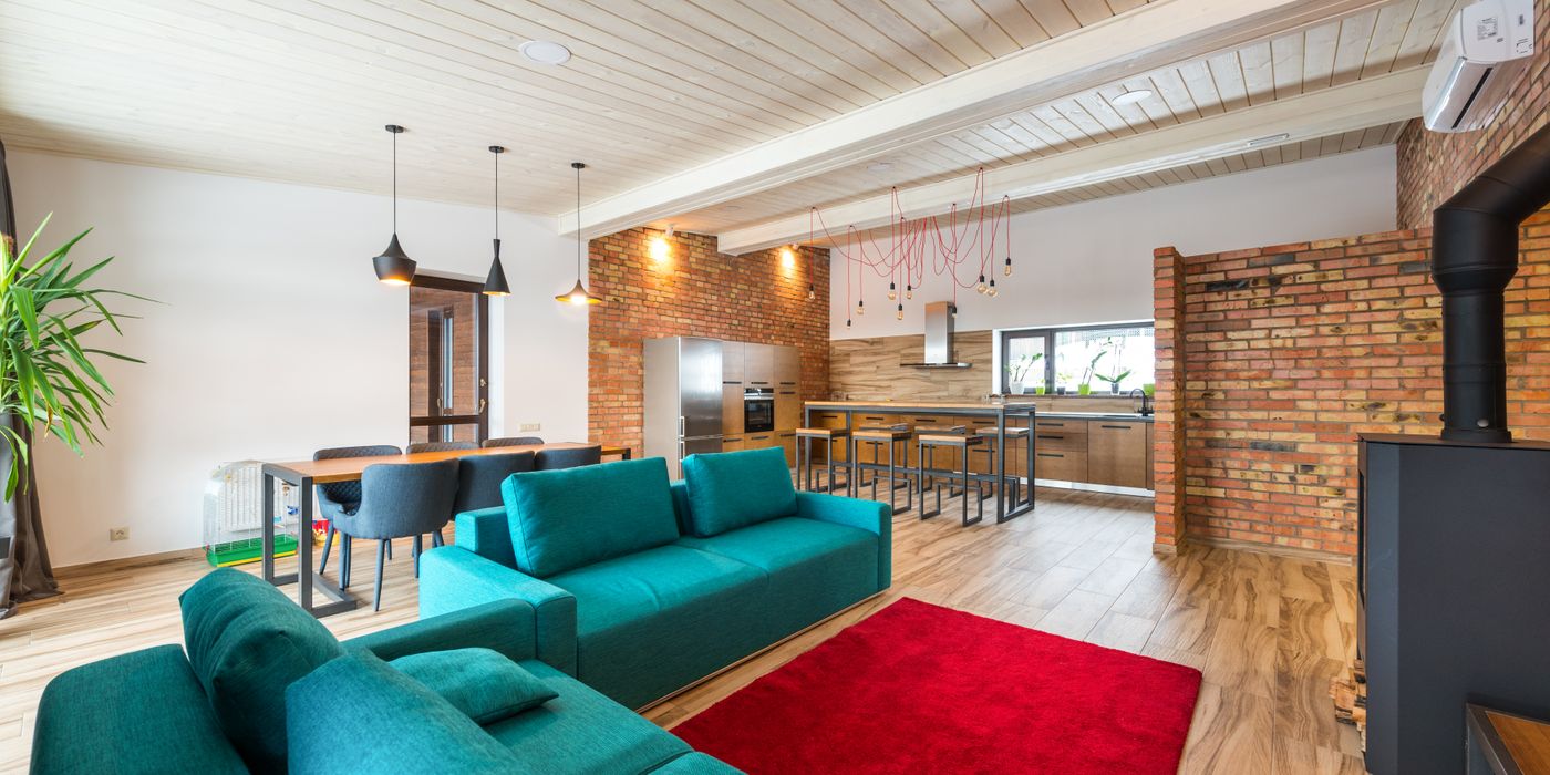 Spacious modern living room featuring brick walls, teal sofa, and red rug.