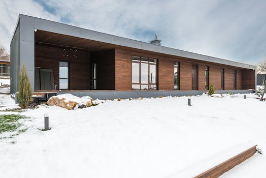 A sleek modern wooden house stands surrounded by a snowy winter landscape, showcasing contemporary architecture.