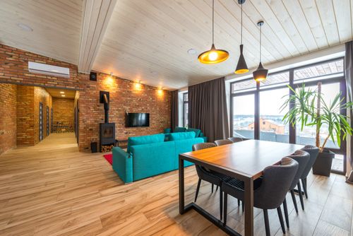 Free Spacious living room featuring brick walls, teal sofa, and large windows overlooking urban scenery. Stock Photo