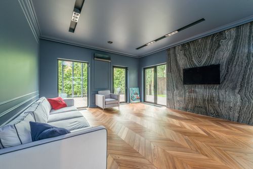 Free Spacious living room with marble wall, chevron wooden flooring, and ample natural light. Stock Photo