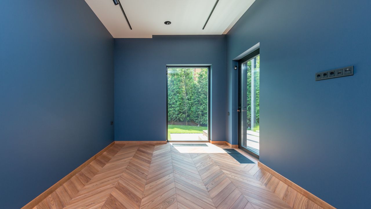 Empty room with an oak herringbone floor and glass doors to a garden