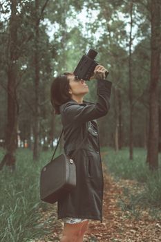 A woman uses a vintage camera in a serene forest setting.