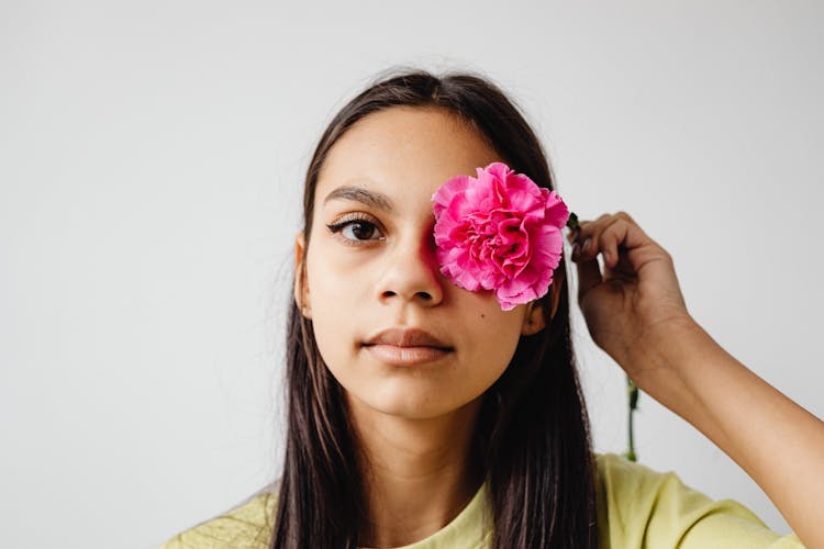 Portrait Of A Teenage Girl Holding A Pink Flower Against Her Eye