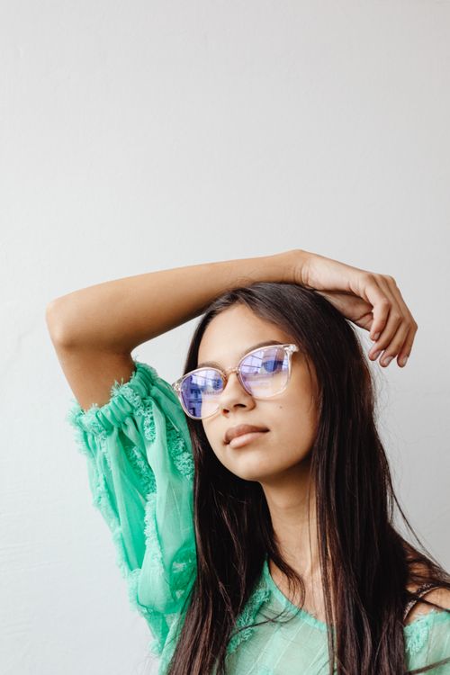 Free Portrait of a fashionable woman with eyeglasses, posing with a hand on her hair against a white backdrop. Stock Photo