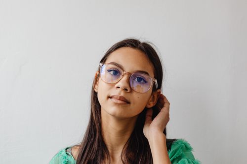 Free A thoughtful young woman wearing eyeglasses, posing indoors against a light background. Stock Photo