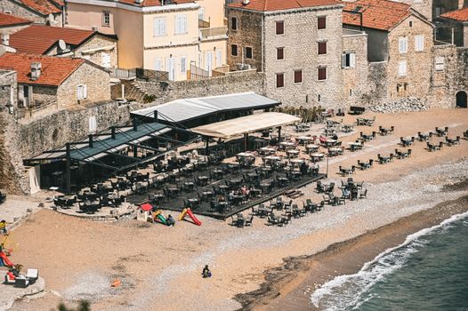 Aerial view of an empty beachfront café and historic stone buildings by the seashore.