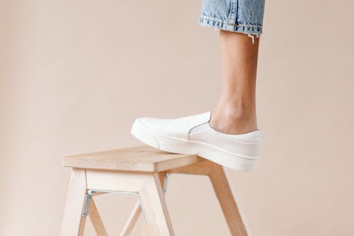 Free Person's Foot Wearing a White Shoes Stepping on a Wooden Stool Stock Photo