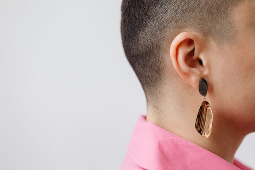 Close-up profile of a woman with a buzzcut wearing a sleek earring on a white background.