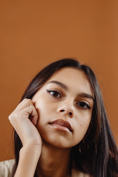 Free Close-up portrait of a stylish young woman posing against a brown background. Stock Photo