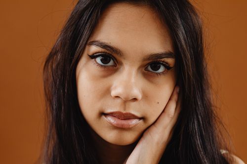 Free Close-up headshot of a woman with long dark hair against an orange background. Stock Photo